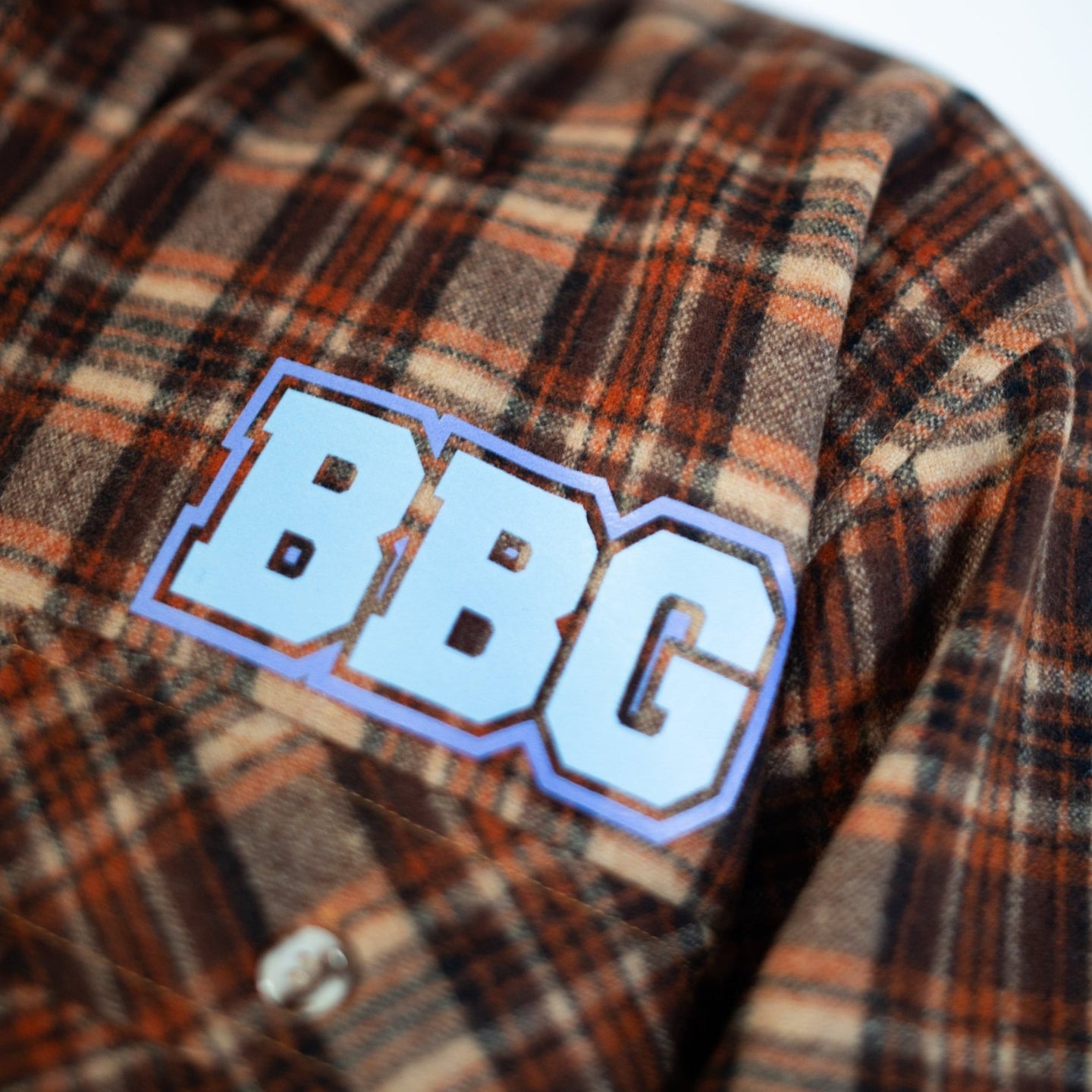 Plaid shirt with 'BBG' logo worn by a person, blurred background