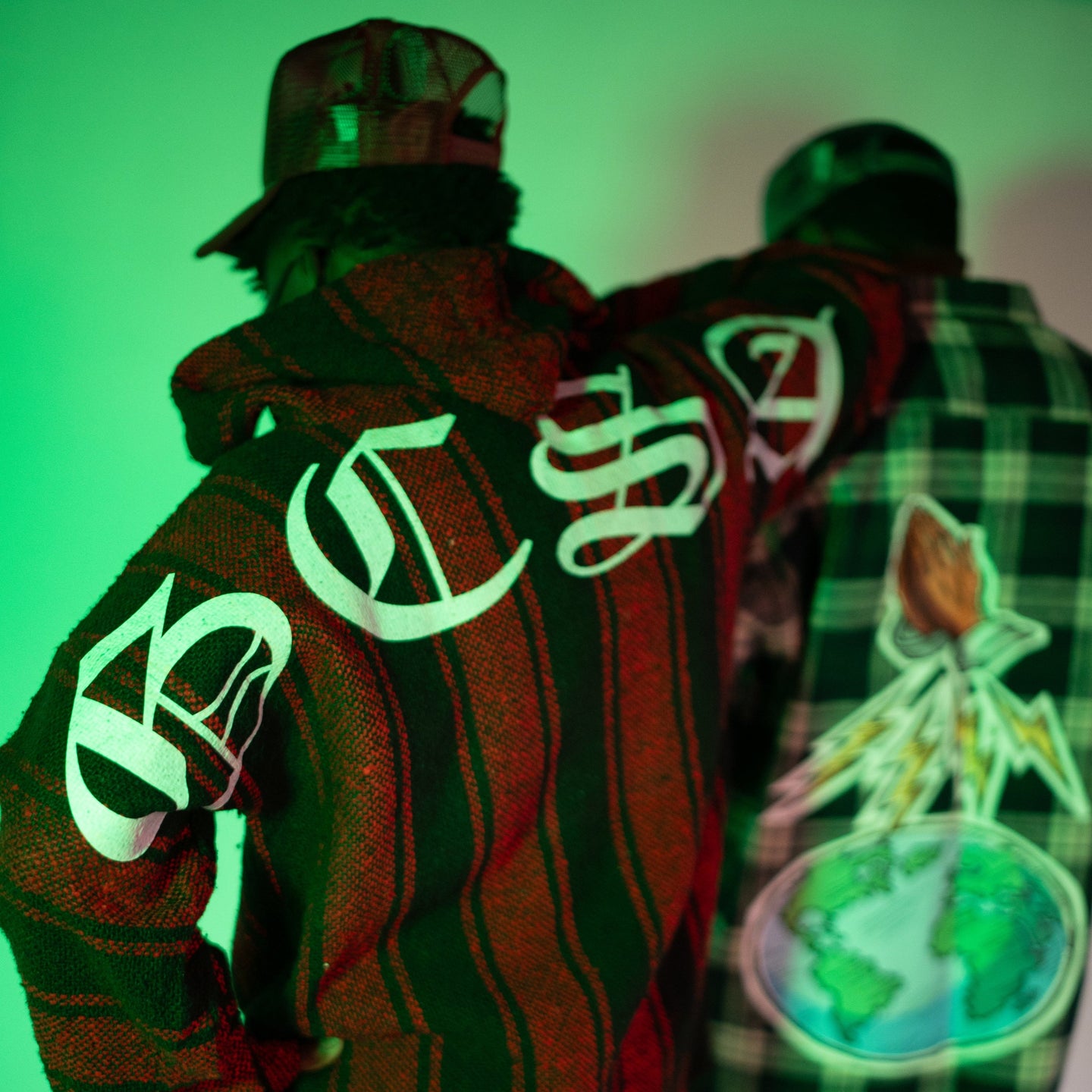 Two people wearing jackets with glowing text and designs against a green background